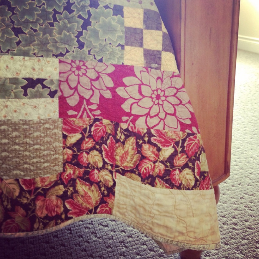 Photo of handmade quilt corner hanging off a bed with a wooden bedpost